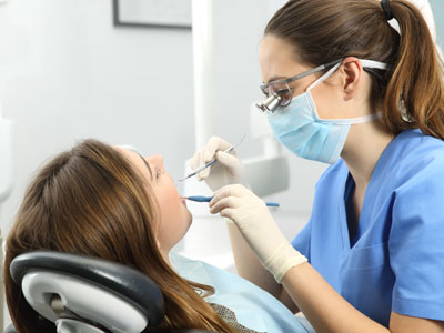 The image shows a dental hygienist working on a patient s teeth while wearing personal protective equipment.